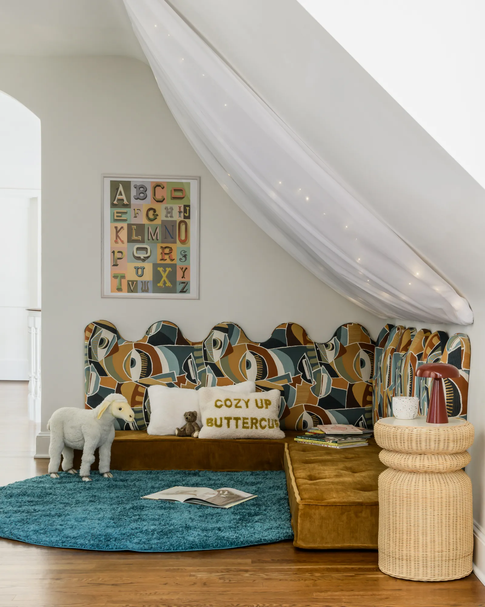 Whimsical children's reading nook with patterned upholstered banquette, sheer canopy, and alphabet art