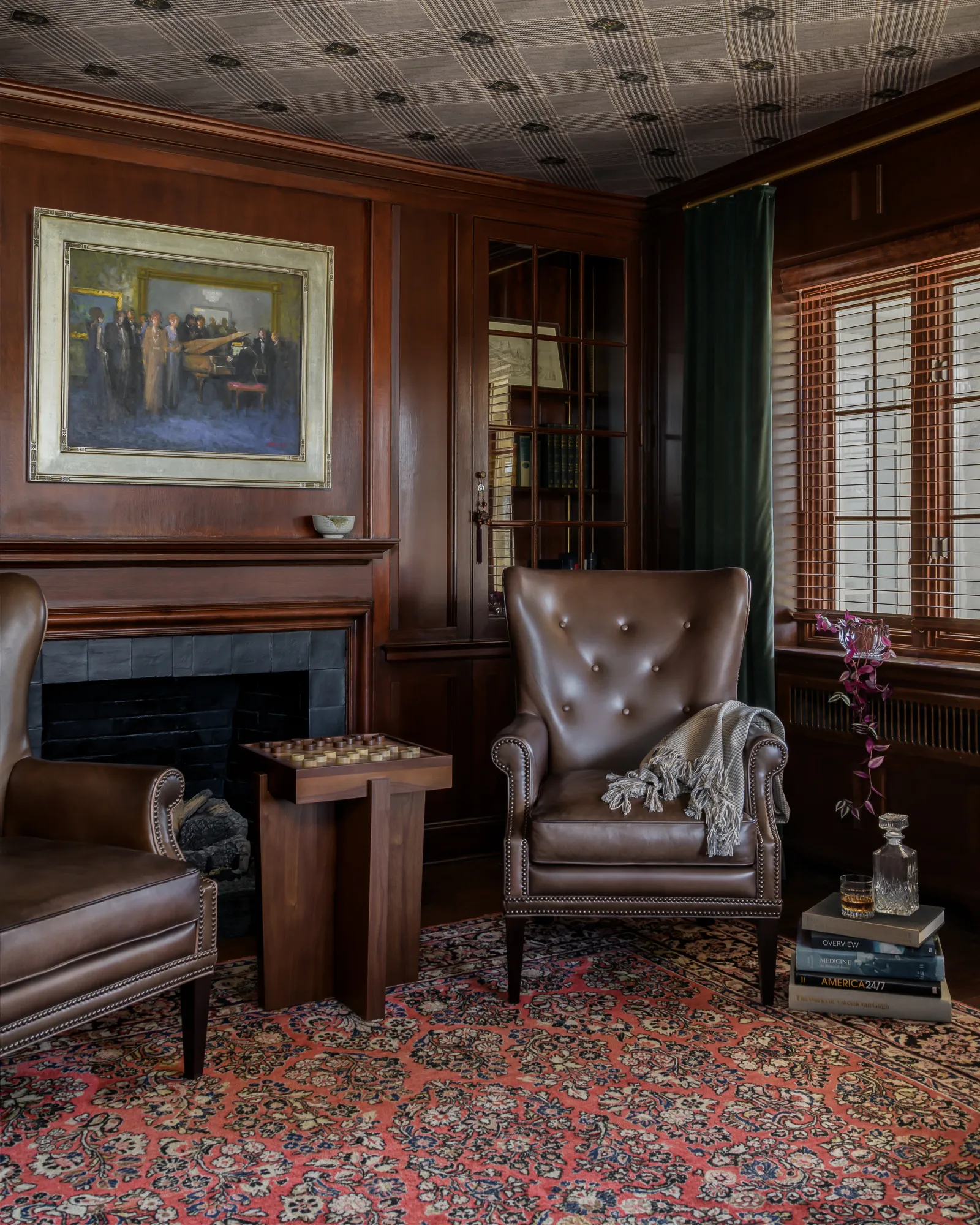Library fireside with tufted wingback chair, chess table, and Persian rug