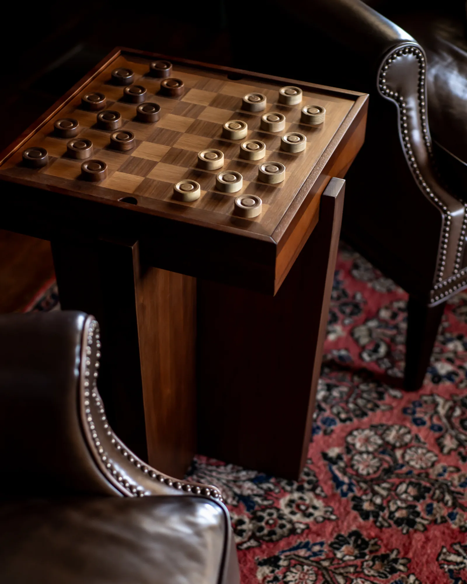Walnut checkerboard game table between leather club chairs