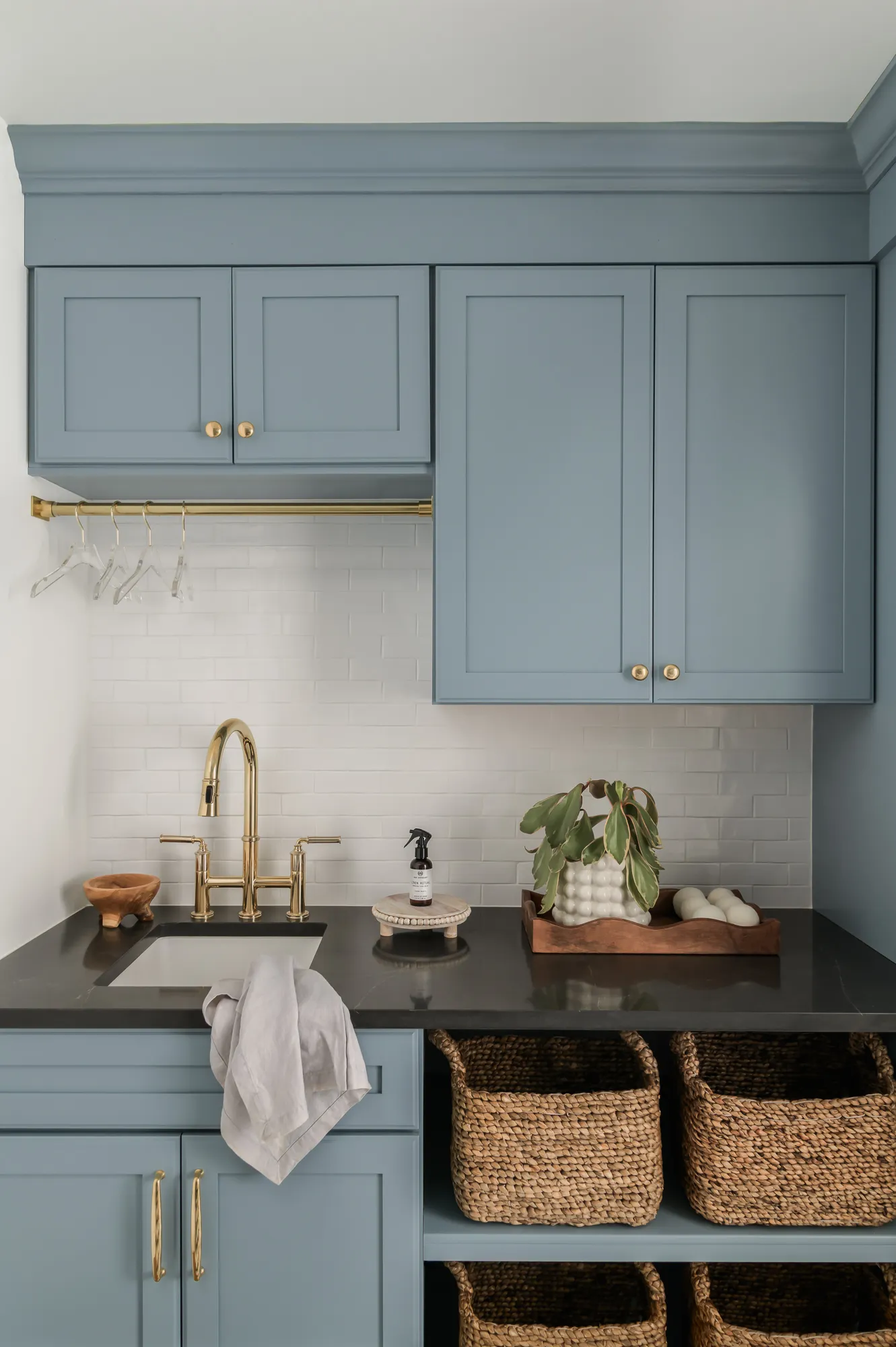 Laundry sink detail with brass bridge faucet, subway tile, and woven baskets