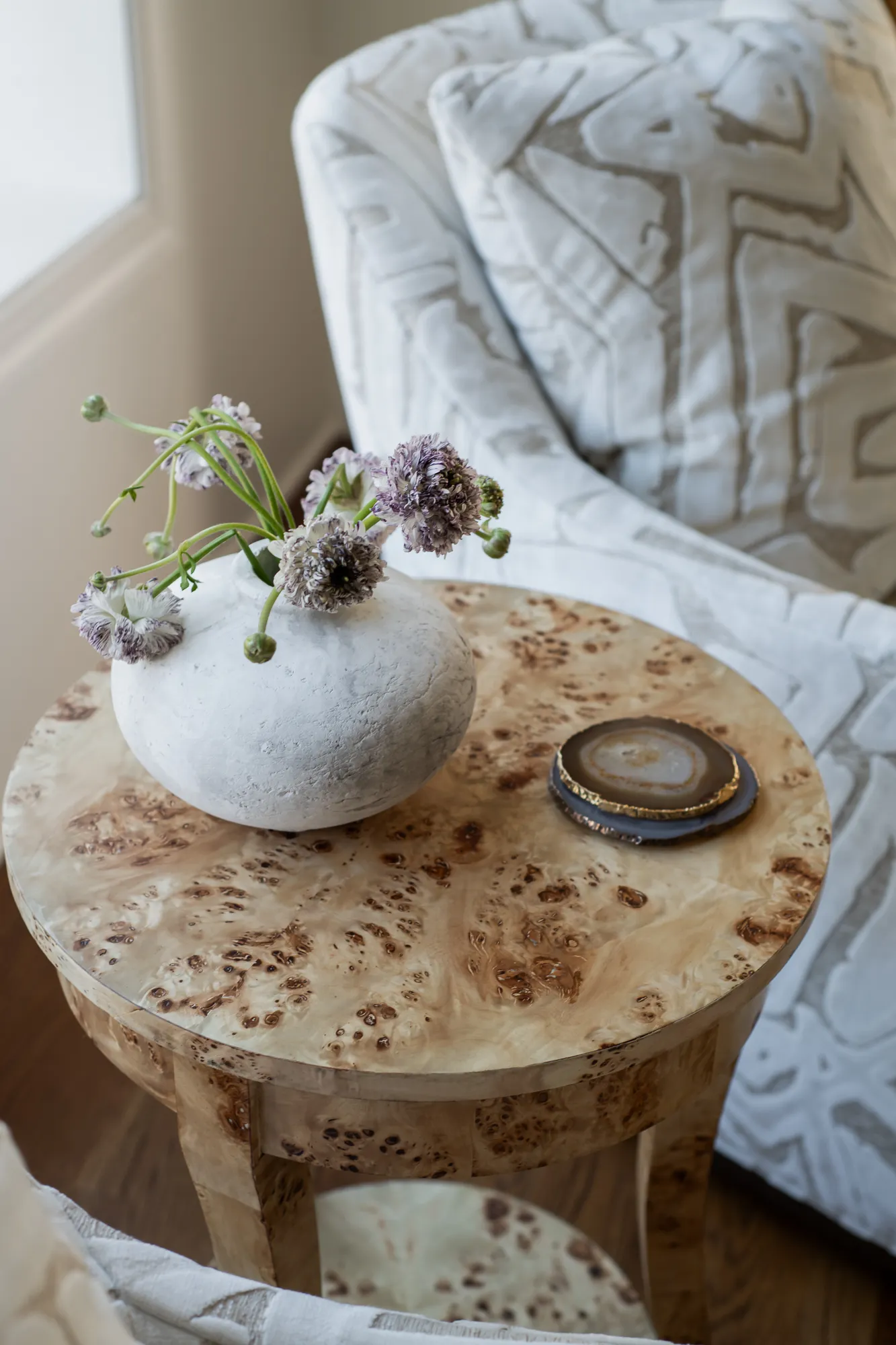 Burled wood side table with stone vase, scabiosa flowers, and agate coasters