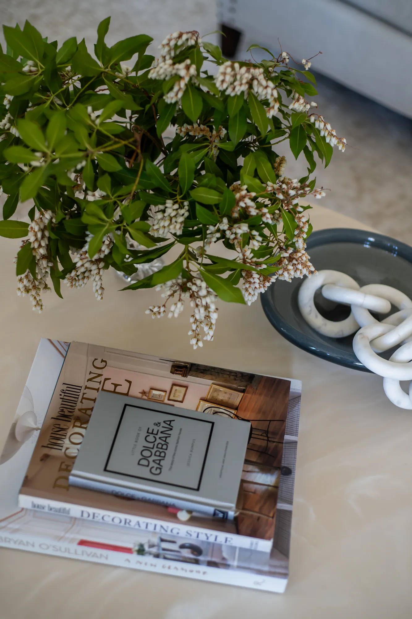 Coffee table vignette with design books, flowering branch, and marble chain sculpture