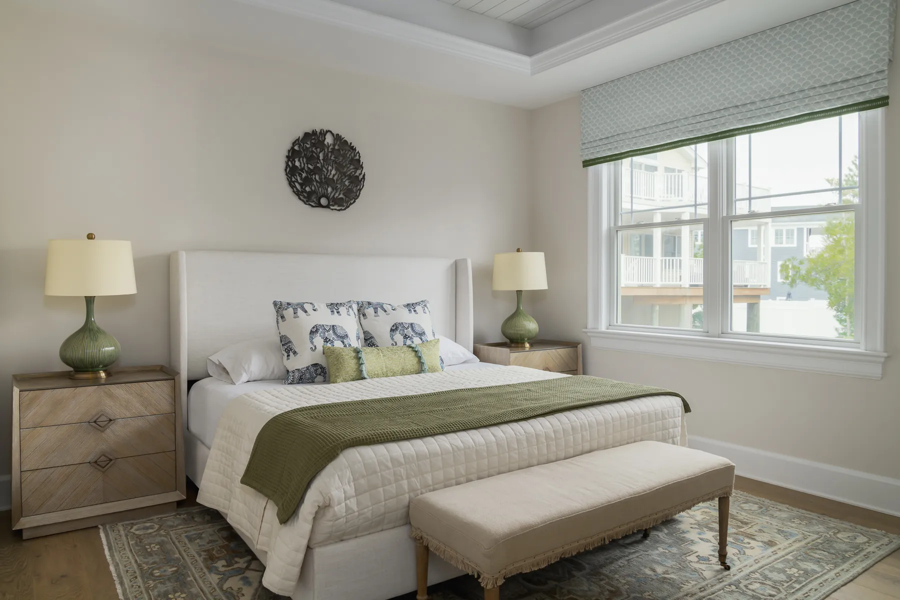 Guest bedroom with sage accents, elephant-print pillows, and coral wall sculpture