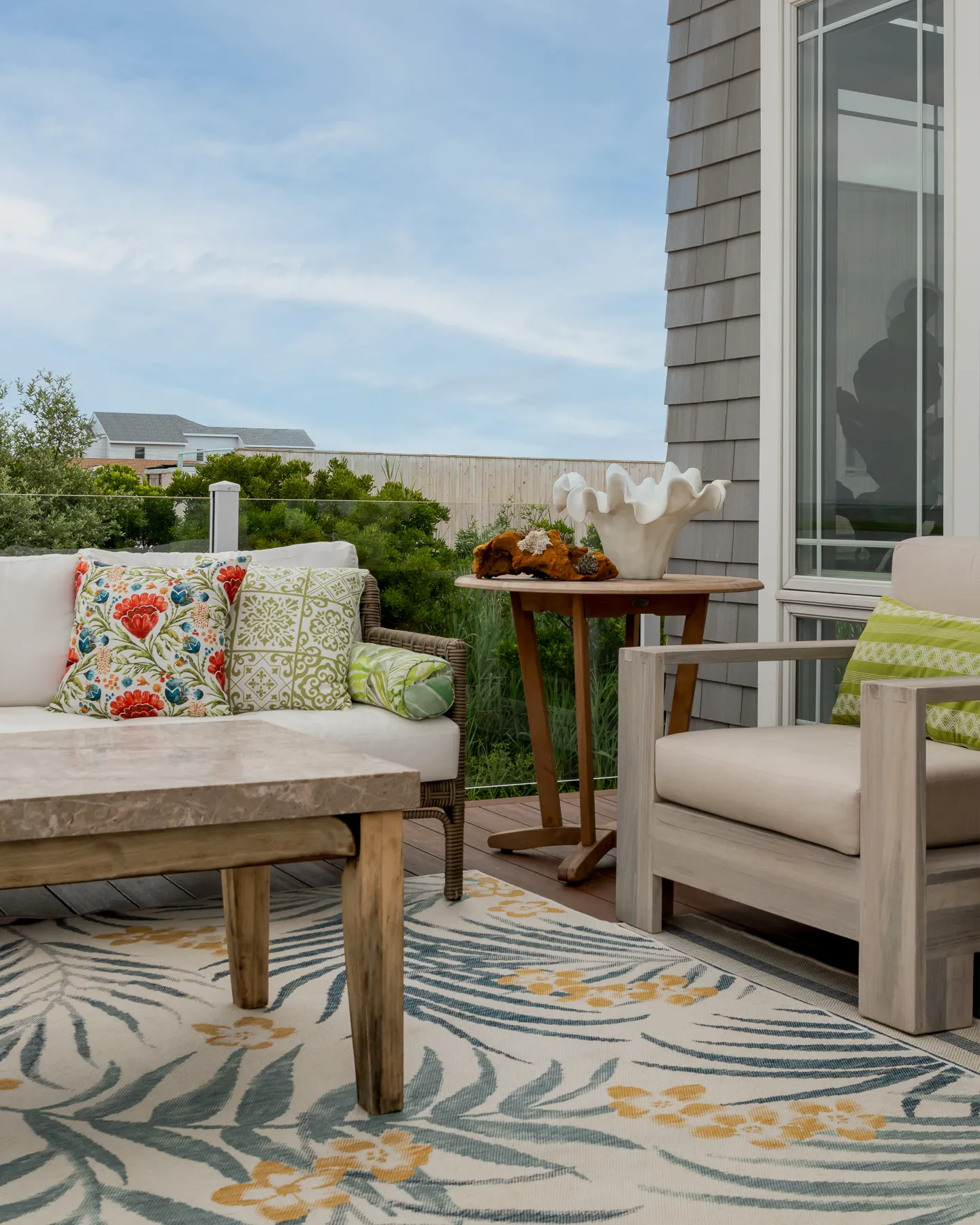 Outdoor vignette with tropical print pillows, ruffled shell sculpture, and palm-leaf rug