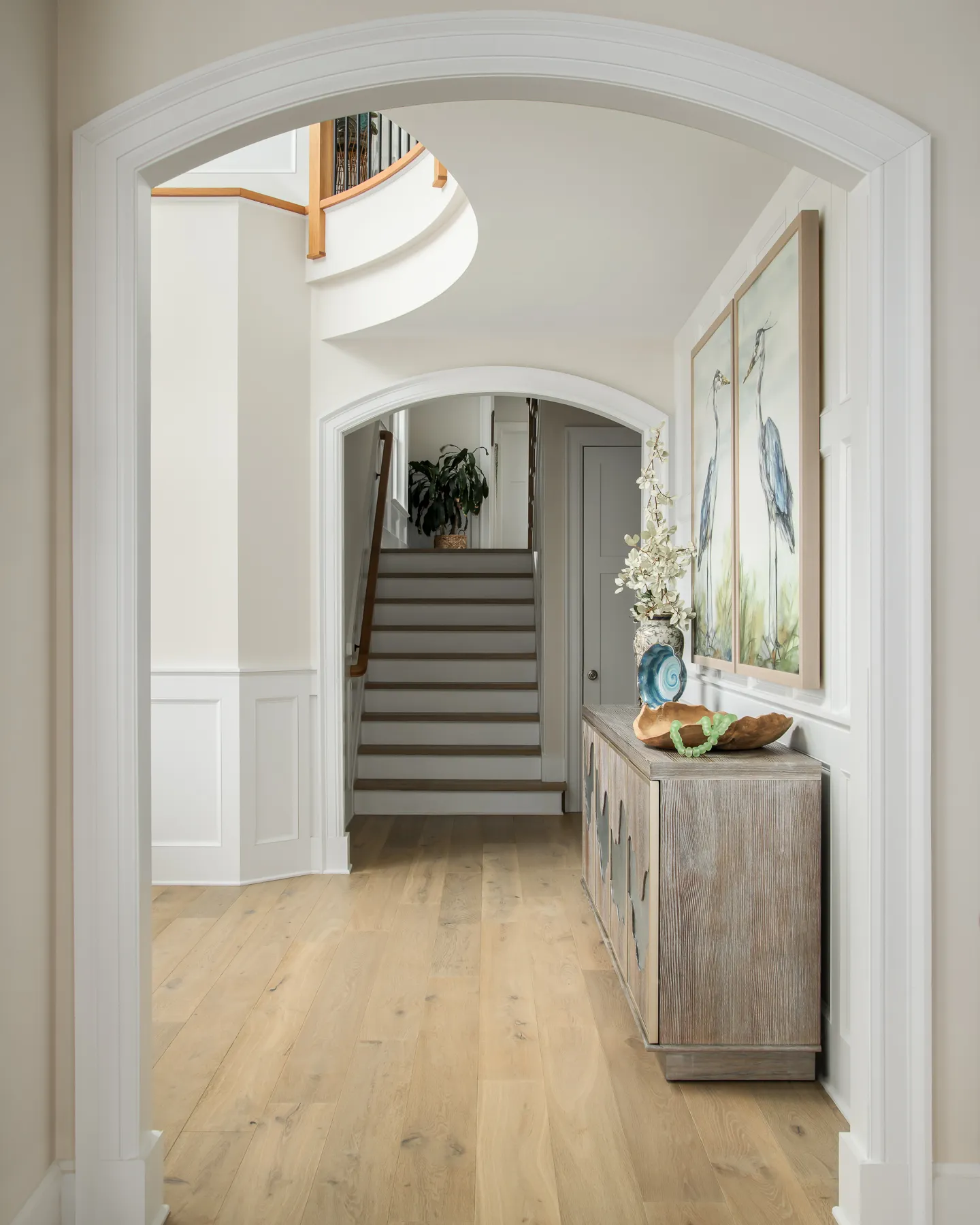 Arched doorway framing the curved staircase, wainscoting, and wave-inlay console