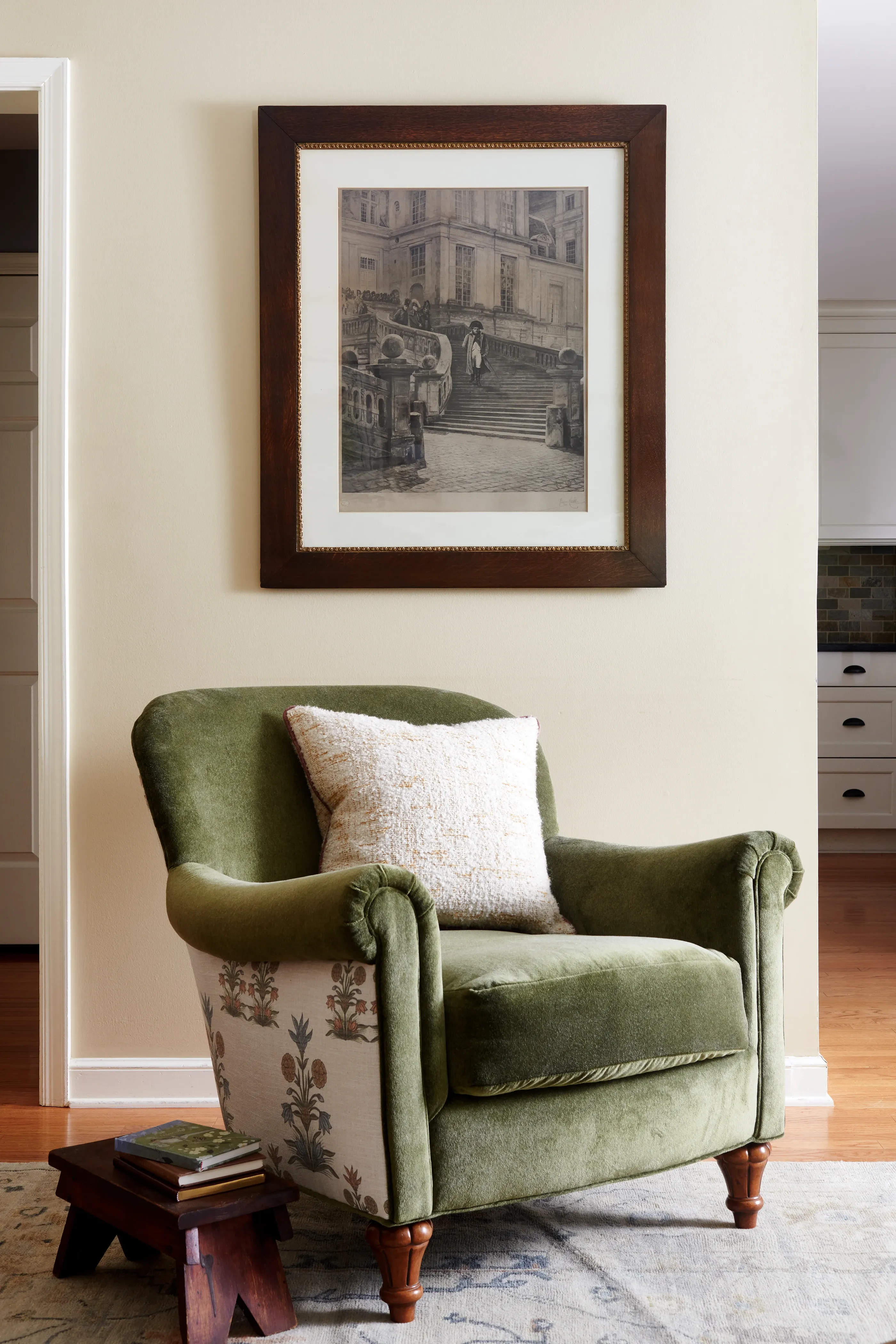 Green velvet rolled-arm chair with floral toile back beneath a sepia European photograph