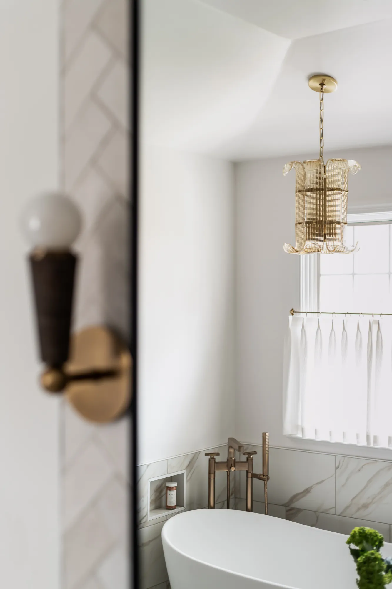 Tub and gold pendant seen through vanity mirror with sconce