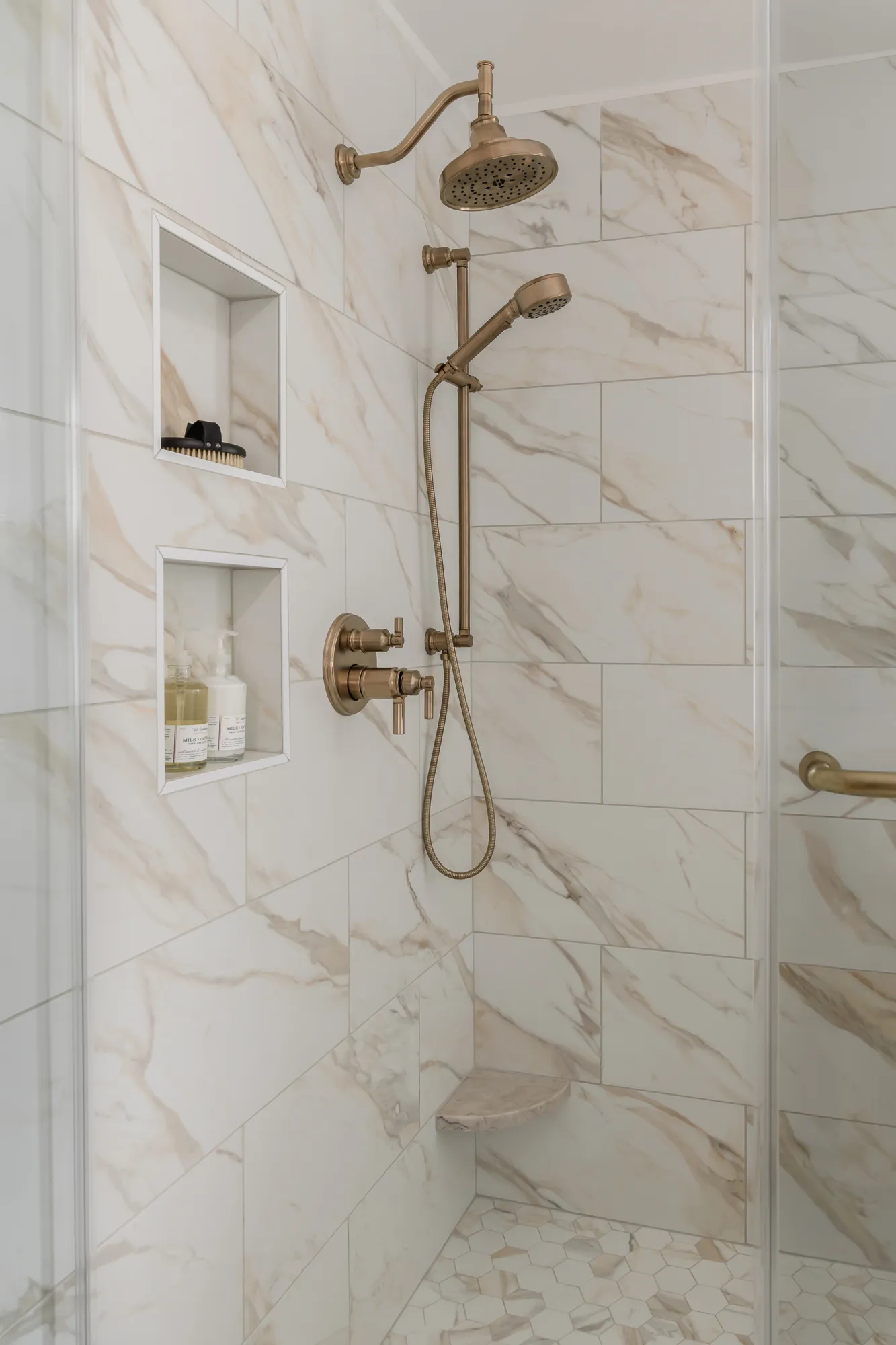 Walk-in shower with marble tile, brass rain shower, and built-in niches